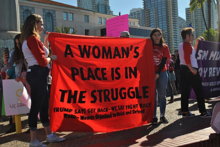 Two women holding a red sign that says, "A woman's place is in the struggle." Other women in the back.